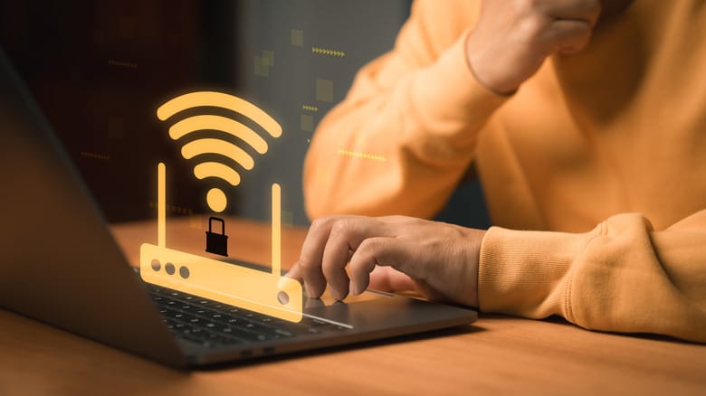 Человек работает за ноутбуком с наложенной графикой Wi-Fi роутера и замка безопасности